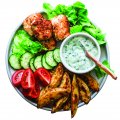 Fish skewers, baked potatoes, vegetables and yogurt greens sauce on dark background, top view