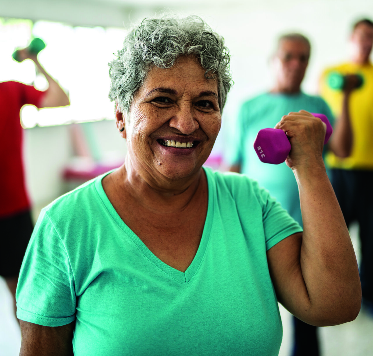 Portrait of senior woman lifting weights with classmates at the gym